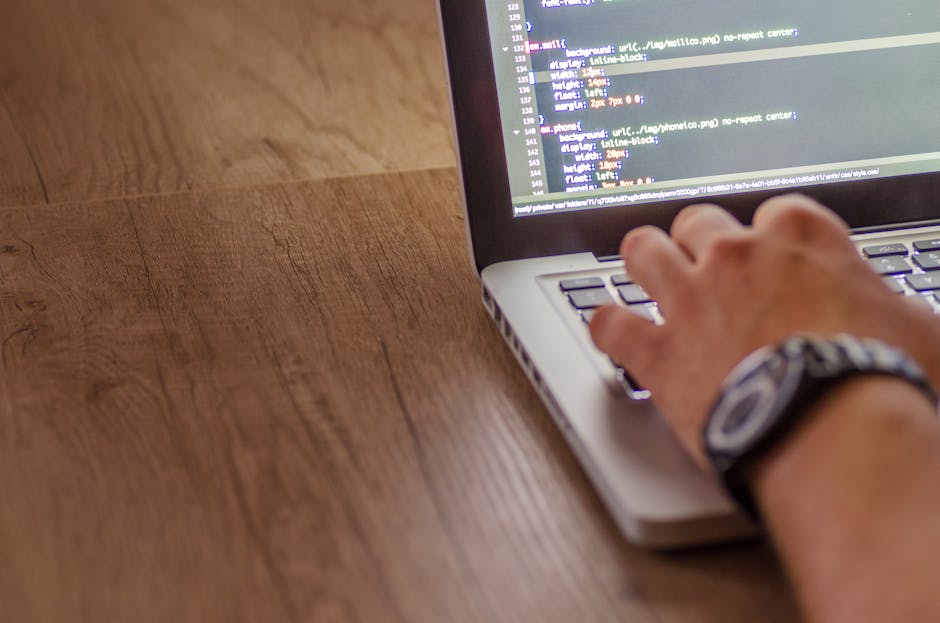 A laptop positioned on a wooden surface displaying lines of code on its screen, next to a ceramic coffee mug with the words 'This coffee is making me awesome' printed in large, dark text. The backgrou